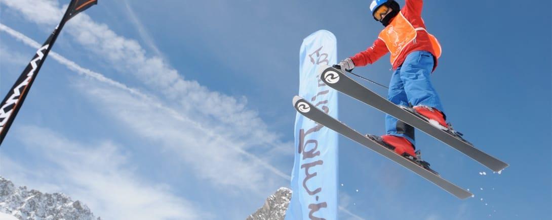 Kind maakt een sprong op ski's tegen een blauwe lucht
